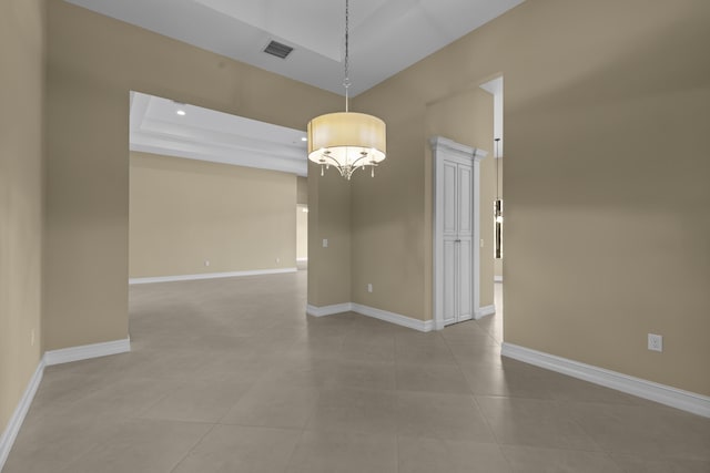 tiled empty room featuring a chandelier and a raised ceiling