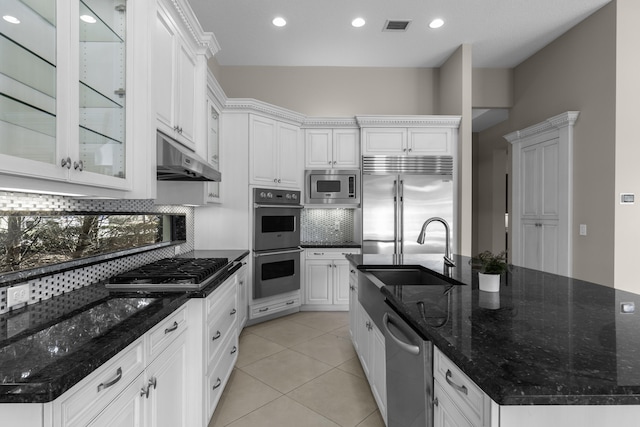 kitchen with sink, dark stone countertops, white cabinets, built in appliances, and a center island with sink