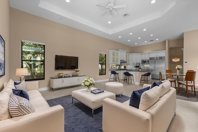 tiled living room featuring a raised ceiling, a healthy amount of sunlight, ceiling fan, and a towering ceiling