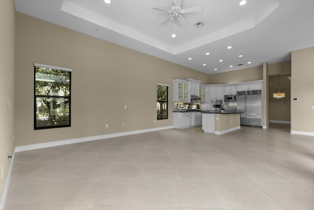 kitchen with a raised ceiling, built in appliances, white cabinets, and light tile patterned floors