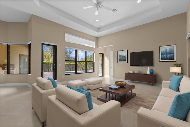 tiled living room with a tray ceiling and ceiling fan