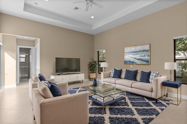 tiled living room featuring ceiling fan, a tray ceiling, and a wealth of natural light