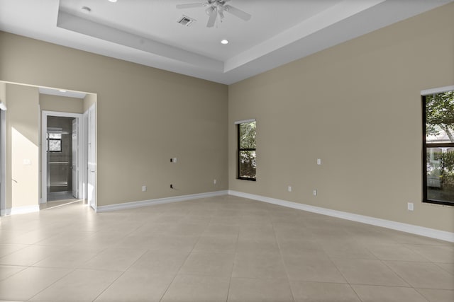 tiled spare room featuring ceiling fan, a tray ceiling, and a wealth of natural light