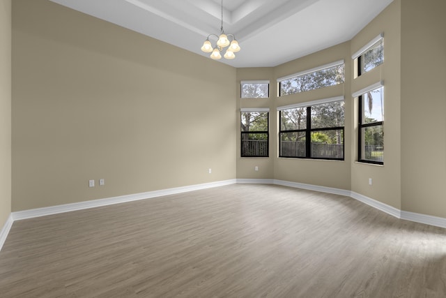 unfurnished room with a tray ceiling, light wood-type flooring, and a notable chandelier