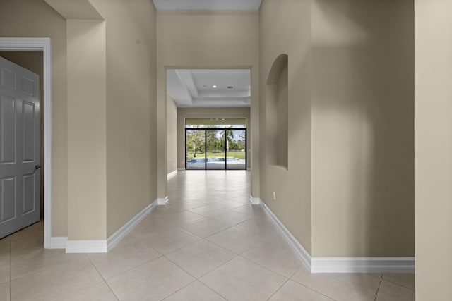 hallway with a tray ceiling and light tile patterned flooring