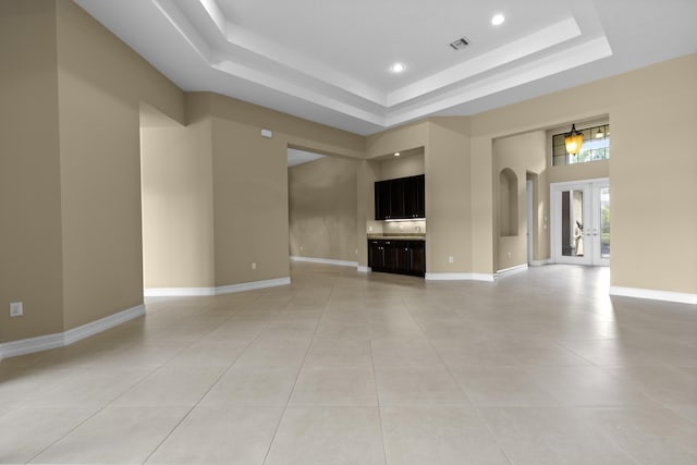 unfurnished living room with french doors, a tray ceiling, light tile patterned flooring, and a high ceiling