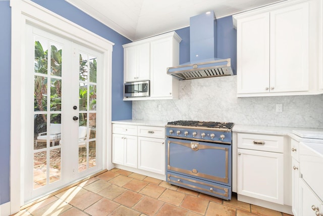 kitchen with white cabinets, wall chimney exhaust hood, appliances with stainless steel finishes, and tasteful backsplash