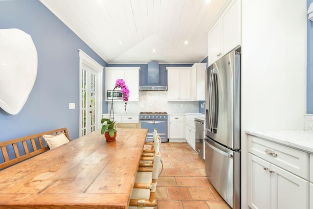 kitchen featuring white cabinets, wall chimney range hood, vaulted ceiling, decorative backsplash, and appliances with stainless steel finishes