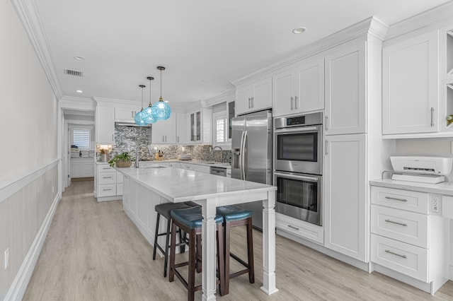 kitchen with white cabinetry, sink, stainless steel appliances, pendant lighting, and ornamental molding