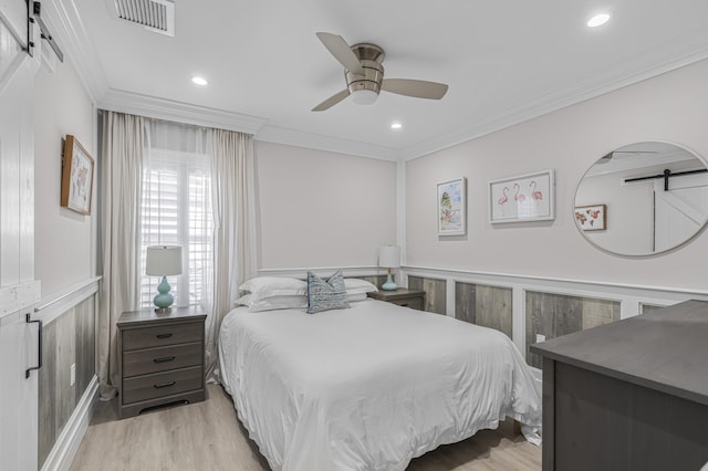 bedroom with ceiling fan, a barn door, crown molding, and light hardwood / wood-style flooring