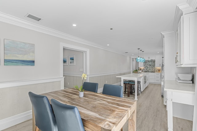 dining space with sink, light hardwood / wood-style floors, and ornamental molding