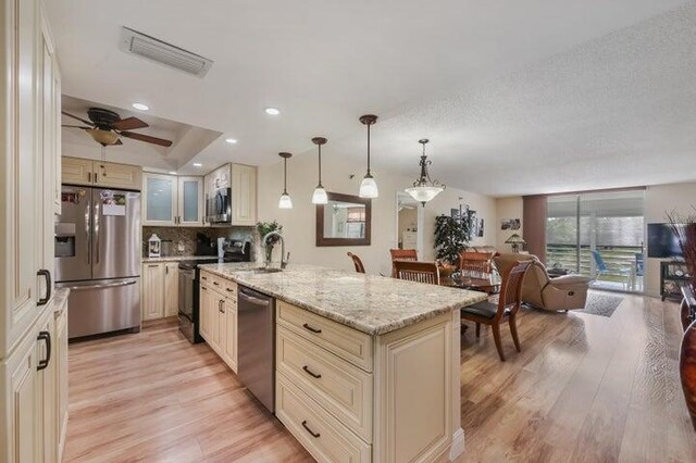 kitchen with cream cabinetry, appliances with stainless steel finishes, light hardwood / wood-style flooring, and light stone counters