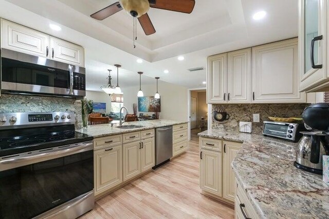 kitchen with pendant lighting, cream cabinets, sink, appliances with stainless steel finishes, and a tray ceiling