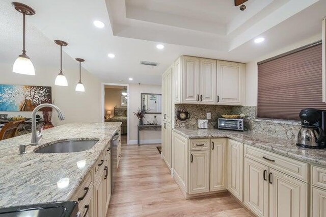 kitchen featuring light stone counters, sink, cream cabinets, light hardwood / wood-style flooring, and hanging light fixtures