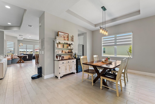 dining space with light wood-type flooring and a tray ceiling