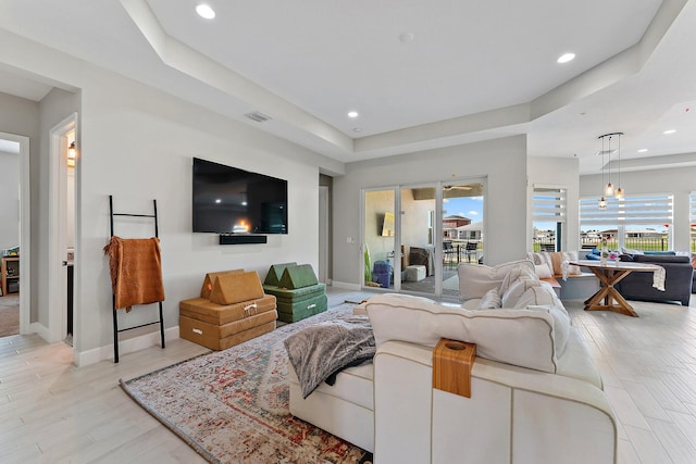 living room featuring plenty of natural light, light wood-type flooring, and a tray ceiling