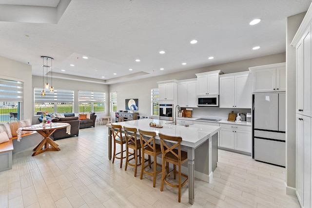 kitchen featuring a kitchen breakfast bar, white cabinetry, a center island with sink, and appliances with stainless steel finishes