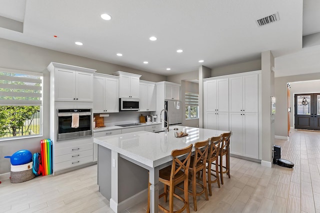 kitchen with light stone countertops, appliances with stainless steel finishes, a kitchen breakfast bar, white cabinetry, and an island with sink