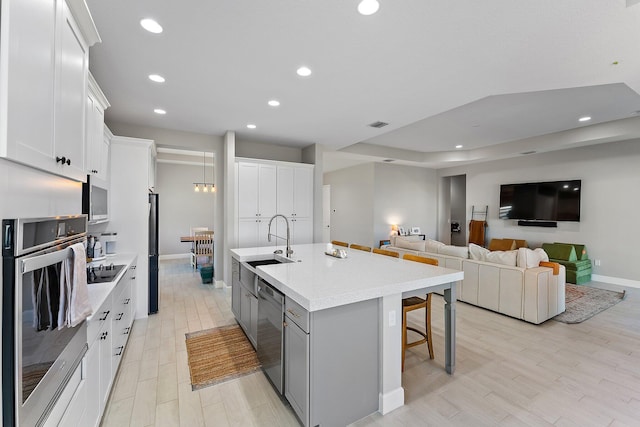 kitchen featuring light hardwood / wood-style flooring, a breakfast bar area, a kitchen island with sink, white cabinets, and appliances with stainless steel finishes