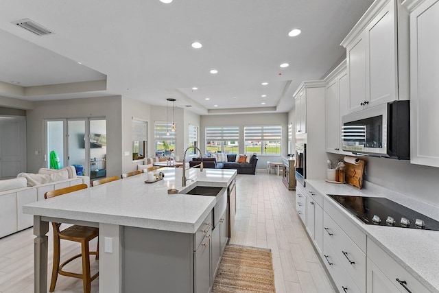 kitchen with white cabinetry, sink, a raised ceiling, black electric cooktop, and a kitchen island with sink