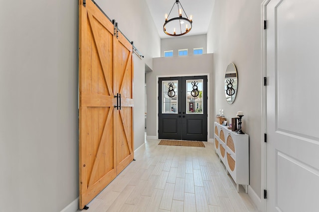 foyer entrance featuring french doors, a high ceiling, a barn door, a chandelier, and light hardwood / wood-style floors