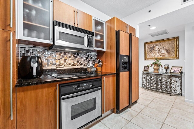 kitchen with dark stone countertops, a textured ceiling, decorative backsplash, light tile patterned flooring, and black appliances