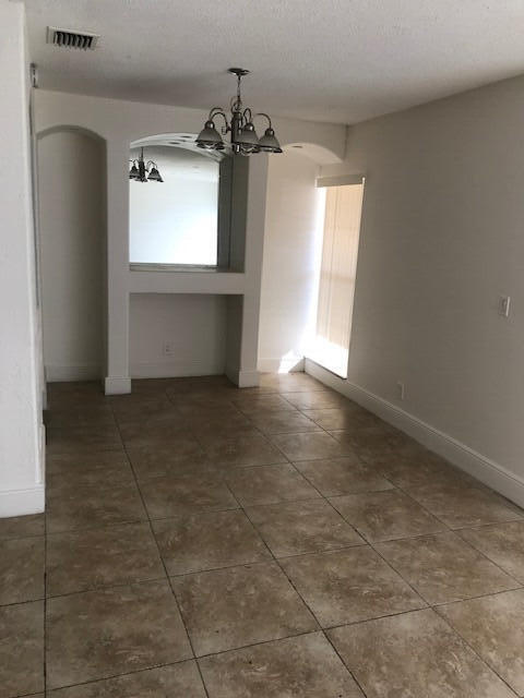 unfurnished dining area with dark tile patterned floors, a textured ceiling, and a chandelier