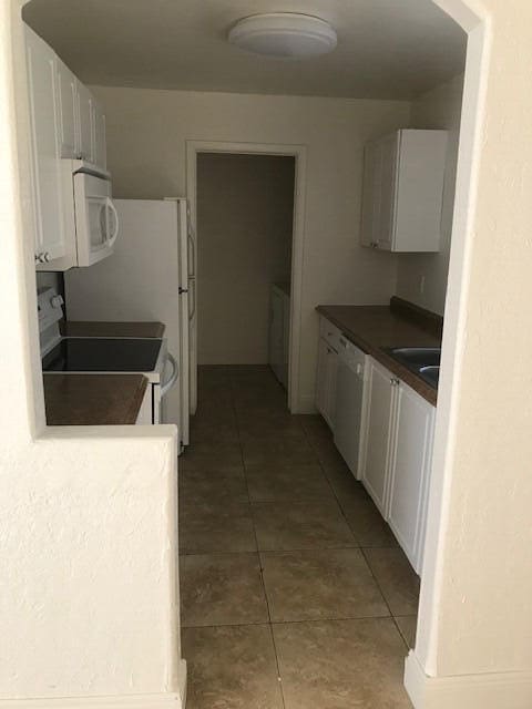 kitchen with tile patterned floors, white appliances, white cabinetry, and sink