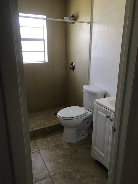 bathroom with tile patterned flooring, vanity, toilet, and a tile shower