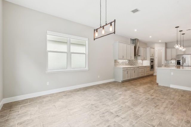 kitchen with appliances with stainless steel finishes, tasteful backsplash, wall chimney exhaust hood, gray cabinetry, and hanging light fixtures