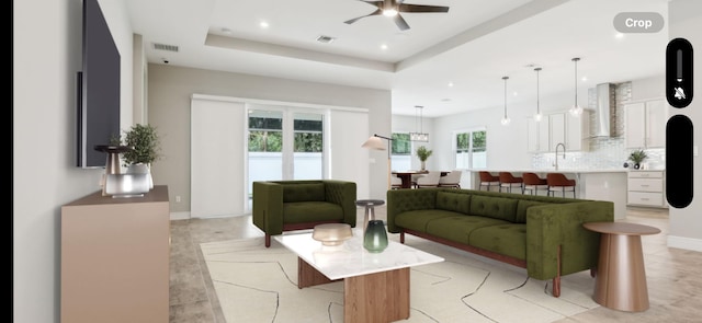 living room with a raised ceiling, ceiling fan, and sink