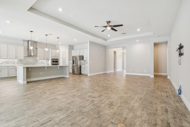 unfurnished living room with a raised ceiling, ceiling fan, and sink