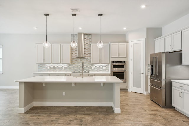 kitchen with wall chimney range hood, stainless steel appliances, and an island with sink