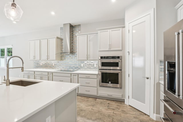 kitchen with sink, wall chimney exhaust hood, pendant lighting, white cabinets, and appliances with stainless steel finishes