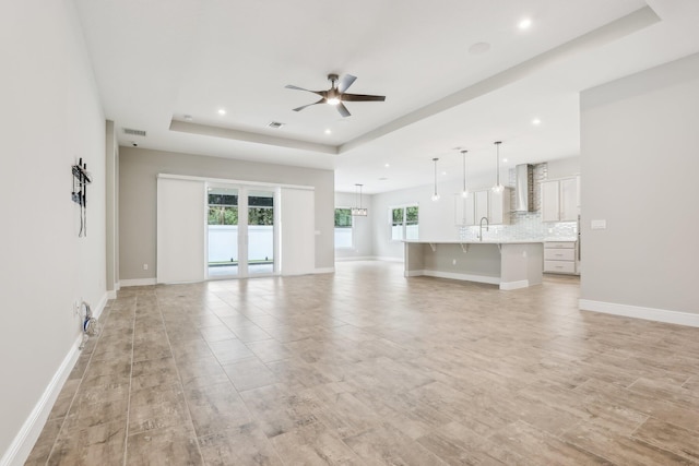 unfurnished living room with light wood-type flooring, a tray ceiling, ceiling fan, and sink