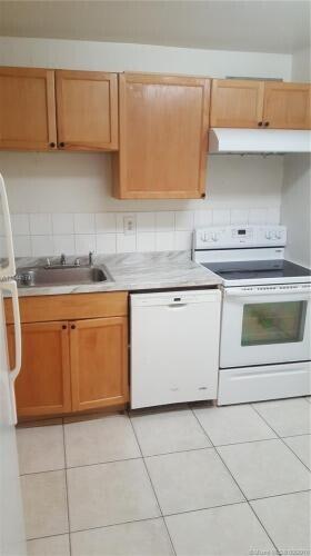 kitchen featuring light tile patterned floors, white appliances, backsplash, and sink