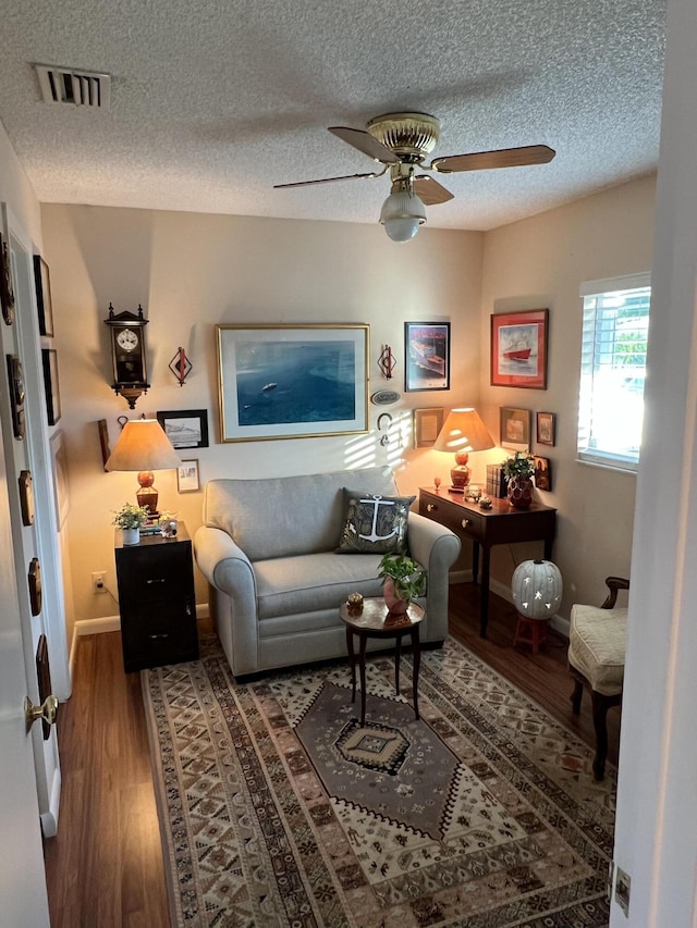 living area featuring ceiling fan, wood-type flooring, and a textured ceiling