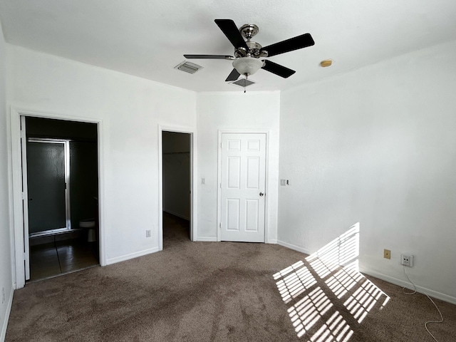 unfurnished bedroom with dark colored carpet, a walk in closet, ensuite bath, ceiling fan, and a closet