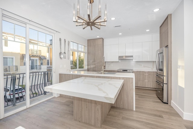 kitchen featuring appliances with stainless steel finishes, sink, light hardwood / wood-style flooring, white cabinets, and an island with sink