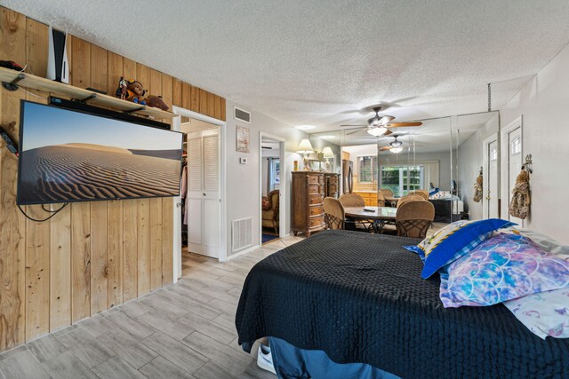 bedroom with wooden walls, wood finished floors, visible vents, and a textured ceiling