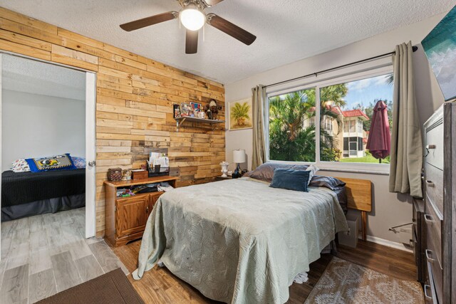 bedroom with ceiling fan, wood walls, light wood finished floors, and a textured ceiling