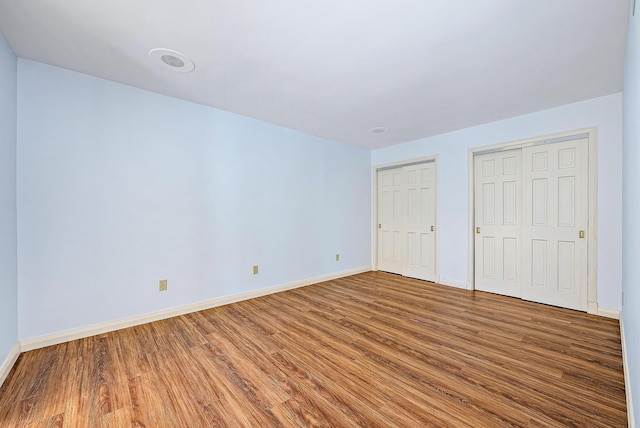 unfurnished bedroom with two closets and hardwood / wood-style flooring