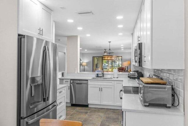 kitchen with kitchen peninsula, decorative backsplash, stainless steel appliances, sink, and white cabinetry