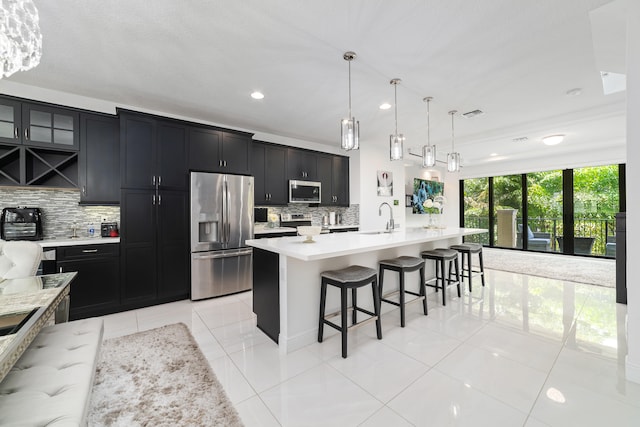 kitchen with pendant lighting, sink, an island with sink, appliances with stainless steel finishes, and tasteful backsplash