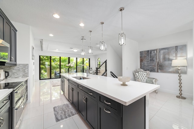 kitchen featuring backsplash, sink, light tile patterned floors, an island with sink, and decorative light fixtures