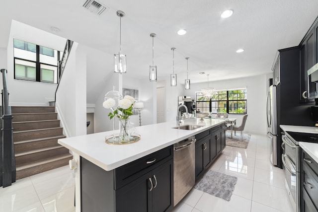 kitchen featuring appliances with stainless steel finishes, sink, a center island with sink, decorative light fixtures, and light tile patterned flooring