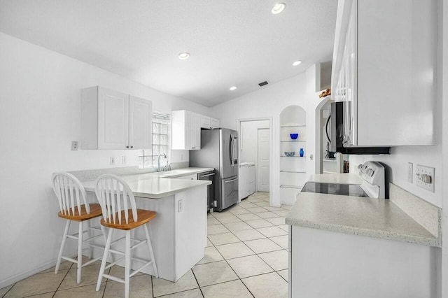 kitchen with kitchen peninsula, lofted ceiling, a kitchen bar, white cabinets, and appliances with stainless steel finishes