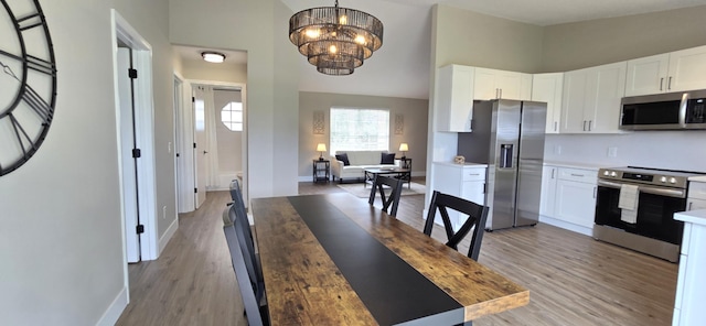 kitchen featuring appliances with stainless steel finishes, a chandelier, white cabinets, light hardwood / wood-style floors, and hanging light fixtures