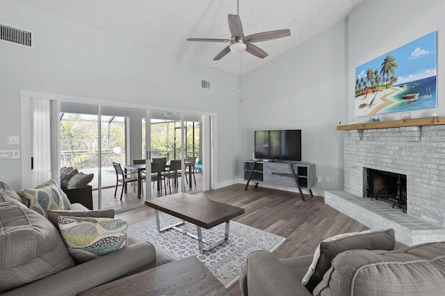 living room featuring hardwood / wood-style floors, high vaulted ceiling, ceiling fan, a fireplace, and a textured ceiling