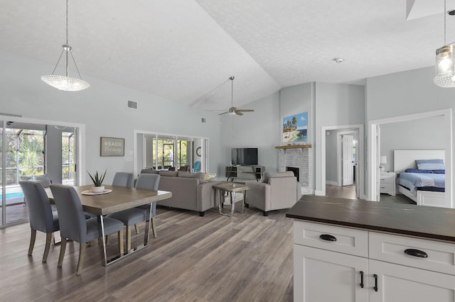 dining room featuring high vaulted ceiling, dark hardwood / wood-style floors, ceiling fan, a textured ceiling, and a fireplace